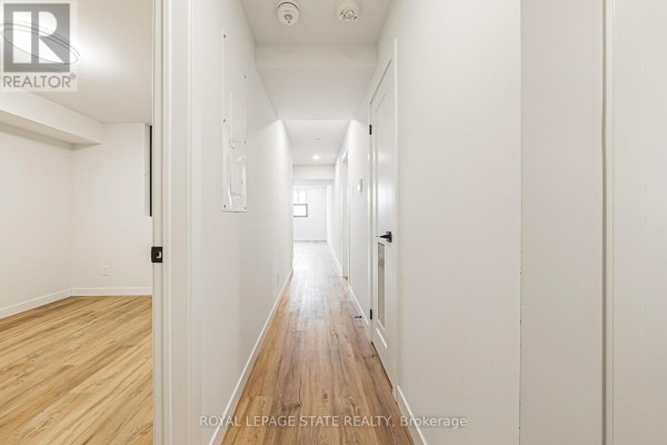 Interior hallway with light wood floors, white walls, and doors leading to rooms. - 102 - 555 Sanatorium Road, Hamilton