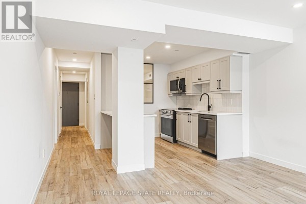 Open concept living area with a galley kitchen featuring light wood floors and white cabinets. - 102 - 555 Sanatorium Road, Hamilton