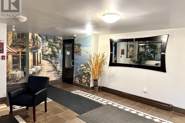 Lobby hallway with a lake mural, a large mirror, and a black armchair. - 102 - 7 Riverview Boulevard, St  Catharines