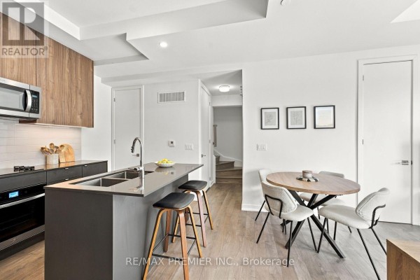 Open concept kitchen and dining area with a gray island, dining table, and staircase. - 102 - 8 Walder Lane, Richmond Hill