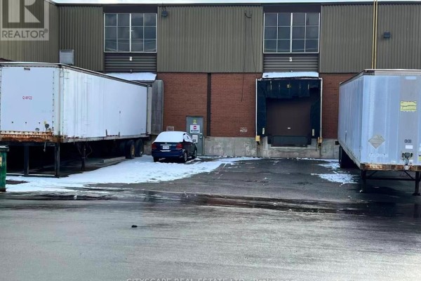 Exterior loading dock area with semi-trailers, a car, and snow on the ground, with two large bay doors. - 102 - Opt C - 100 Steelcase Road E, Markham