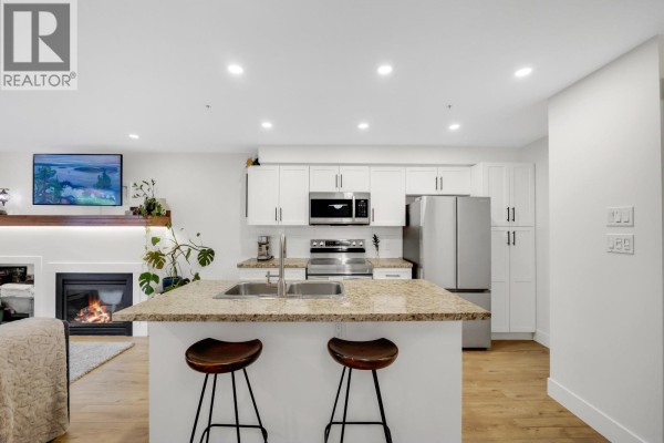 Kitchen island with granite countertop, stainless steel appliances, and seating for two on bar stools. - 102 1174 Wingtip Place, Squamish