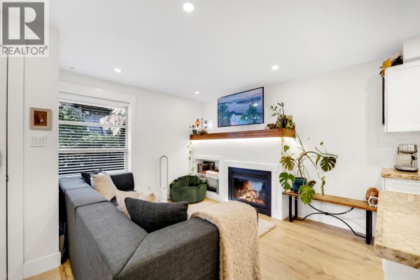 Living room with a grey sectional sofa, gas fireplace, and a television mounted above the mantel. - 102 1174 Wingtip Place, Squamish
