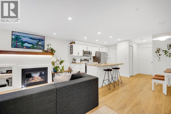 View of the living room fireplace, grey sofa, and open kitchen with white cabinets and stainless steel appliances. - 102 1174 Wingtip Place, Squamish