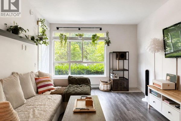 Living room with a sectional sofa, large window with green views, and dark wood floors. - 102 2436 Kelly Avenue, Port Coquitlam