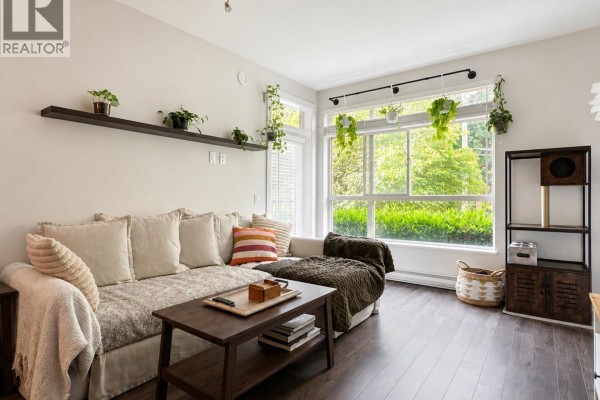 Living room sofa and coffee table facing a large window with green trees outside. - 102 2436 Kelly Avenue, Port Coquitlam