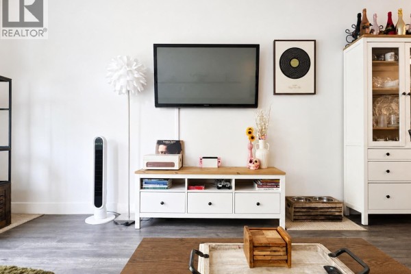 Living room entertainment center with a wall-mounted TV, white cabinet, and decorative items. - 102 2436 Kelly Avenue, Port Coquitlam
