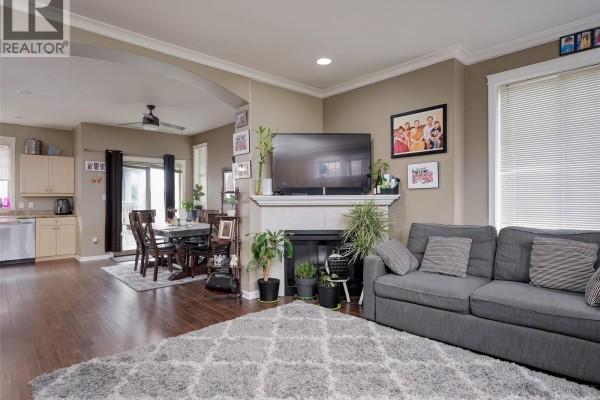 Living room with a grey sofa, fireplace, television, and a dining area in the background. - 102 2923 Phipps Rd, Langford