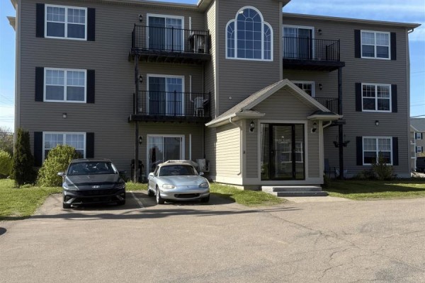 Exterior view of a three-story apartment building with a central entrance and parked cars. - 36 Ducks Landing Unit 102, Stratford
