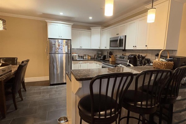 Kitchen with white cabinetry, stainless steel appliances, granite countertops, and bar seating. - 36 Ducks Landing Unit 102, Stratford