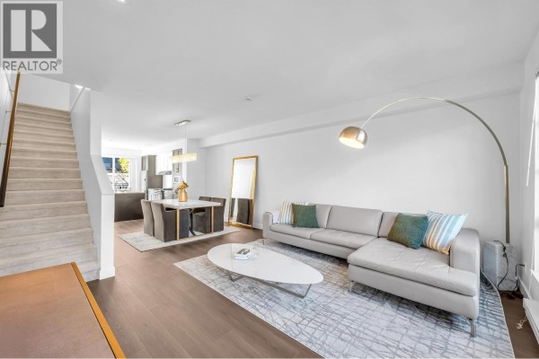 Open concept living and dining area with a sectional sofa, dining set, and a staircase leading upstairs. - 102 548 Foster Avenue, Coquitlam