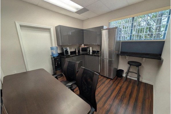 Kitchenette with grey cabinets, stainless steel appliances, a water cooler, and a table with chairs. - 102 5668 192 Street, Surrey