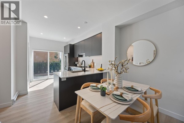 Modern kitchen featuring dark cabinetry, stainless steel appliances, and a large island with seating. - 102 639 Aspen Street, Coquitlam