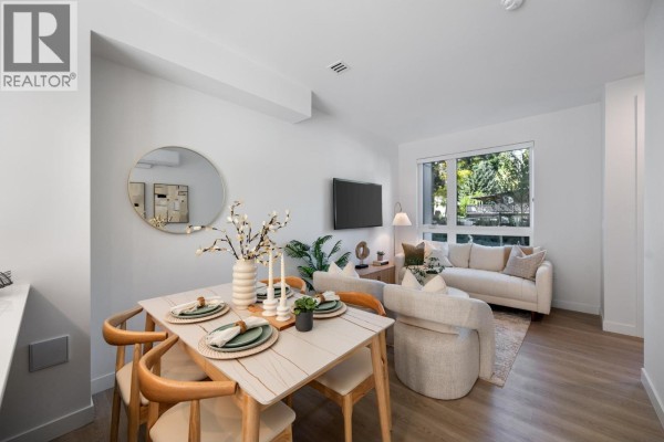 Bright living room with a sectional sofa, dining area, and large windows for natural light. - 102 639 Aspen Street, Coquitlam