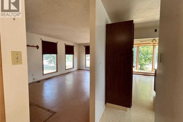 View from hallway into a living room with beige walls and wood-trimmed windows. - 102 6th Avenue W, Eatonia