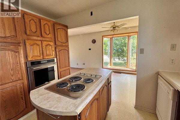 Kitchen island with a stovetop and oak cabinets, looking towards a bay window. - 102 6th Avenue W, Eatonia
