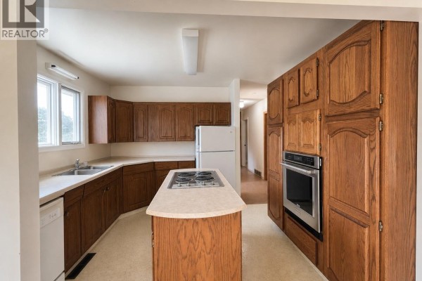 Spacious kitchen with oak cabinets, a stovetop island, white appliances, and a window. - 102 6th Avenue W, Eatonia