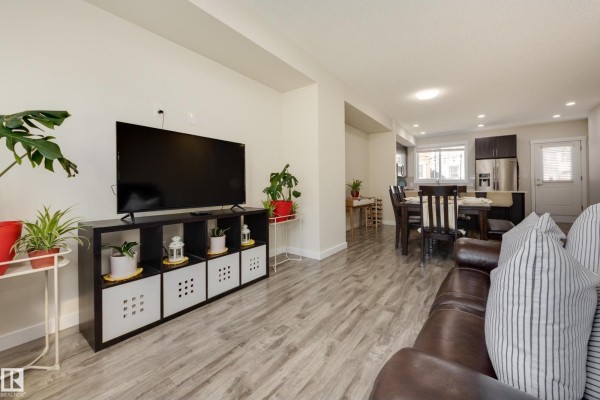 Living room with a large television on a black media stand, and dining area beyond. - #102 903 Crystallina Nera Wy Nw, Edmonton