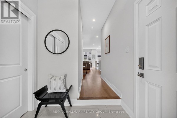 Entryway with light grey walls, hardwood floor, and a black bench with striped cushion. - 102 Aquarium Avenue, Ottawa