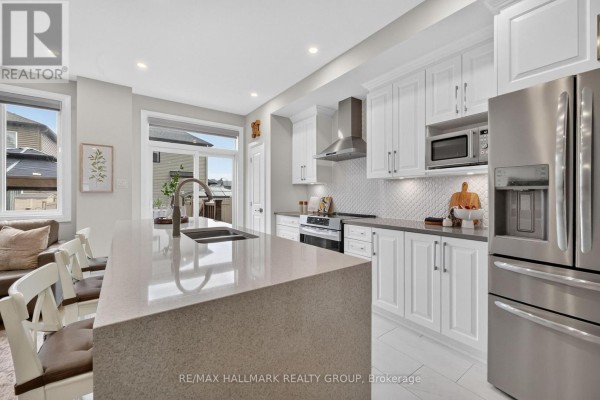 Kitchen with white cabinets, quartz countertops, stainless steel appliances, and island with sink. - 102 Aquarium Avenue, Ottawa