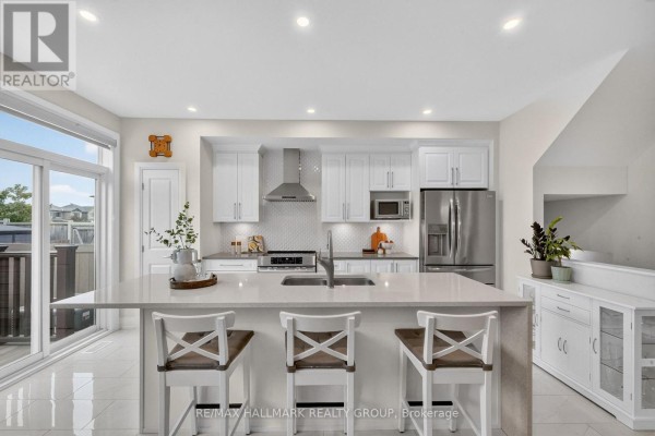 Open-concept kitchen and living area with white cabinetry, island, and large windows. - 102 Aquarium Avenue, Ottawa
