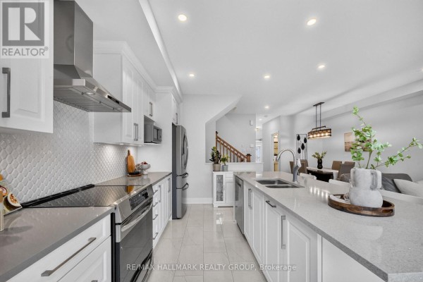 Modern kitchen with white cabinets, grey quartz counters, stainless steel appliances, and island. - 102 Aquarium Avenue, Ottawa