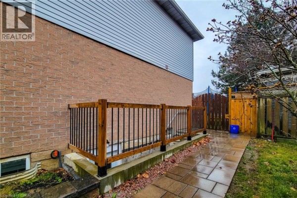 Side view of a brick house showing a wooden deck with black railings and a backyard. - 102 Bonaparte Way Unit# 2 Lower, Hamilton