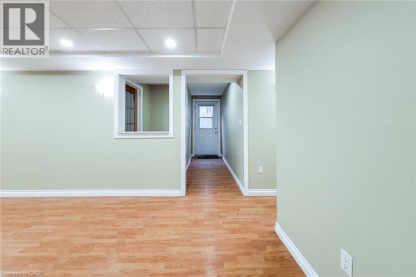 Interior basement hallway with light green walls, wood laminate flooring, and a doorway. - 102 Bonaparte Way Unit# 2 Lower, Hamilton