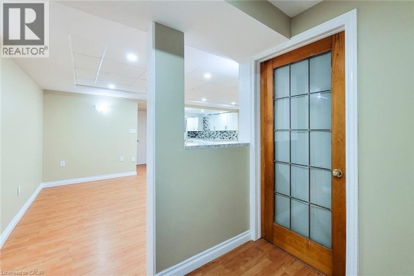 View of an interior room with light green walls, wood laminate flooring, and a glass-paneled wooden door. - 102 Bonaparte Way Unit# 2 Lower, Hamilton