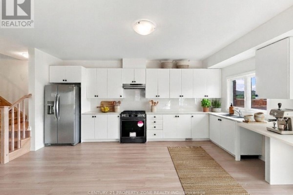 Modern white kitchen with stainless steel appliances, ample cabinet space, and a large window. - 102 Cadillac Crescent, Brampton