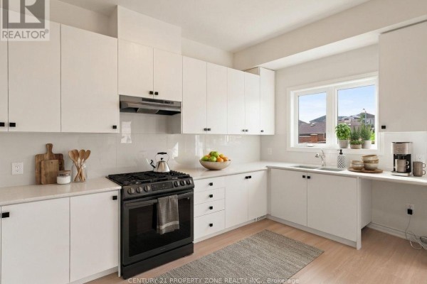 Close-up view of a white kitchen with a black gas stove, white countertops, and a window. - 102 Cadillac Crescent, Brampton