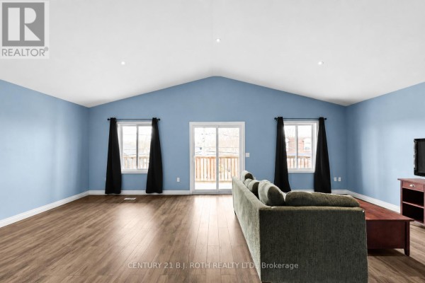 Living room with light blue walls, vaulted ceiling, wood-look flooring, and a sliding glass door. - 102 Dunlop Street, Orillia