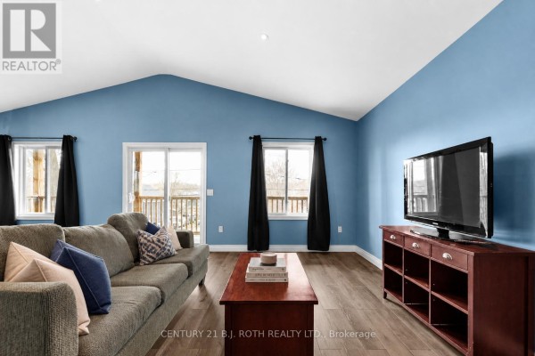 Living room with blue walls, vaulted ceiling, wood floors, sofa, coffee table, and television stand. - 102 Dunlop Street, Orillia