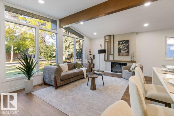 Living room with a sofa, fireplace, large windows, and a partial view of dining area. - 102 Goodridge Dr, St  Albert