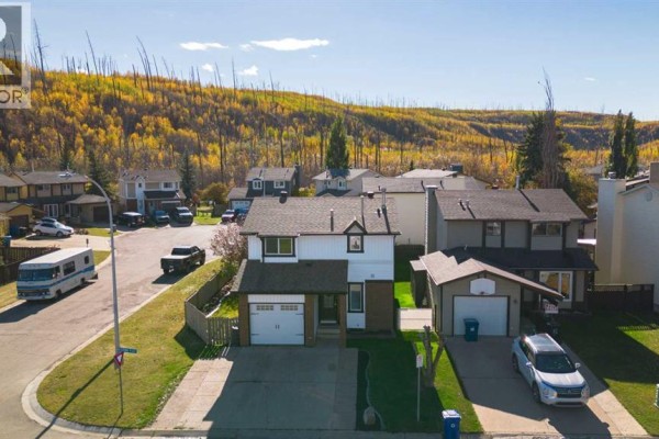 Aerial view of a suburban house with a wooded hillside in the background. - 102 Goodwin Place, Fort Mcmurray