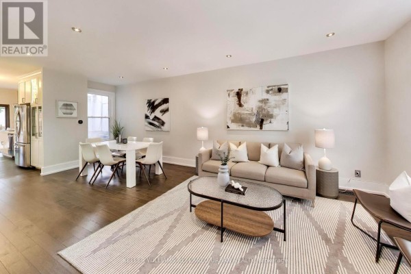 Living room with a large television, white media console, dark hardwood floors, and a grey couch. - 102 Gough Avenue, Toronto