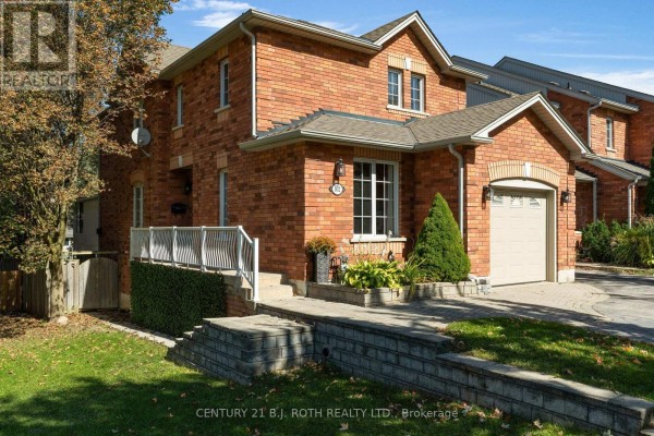 Close-up of the brick townhouse exterior with a white-railed porch and stone retaining wall. - 102 Holgate Street, Barrie