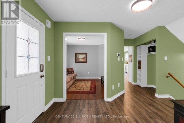 Foyer with green walls, wood-look flooring, and an entryway into a living area. - 102 Holgate Street, Barrie