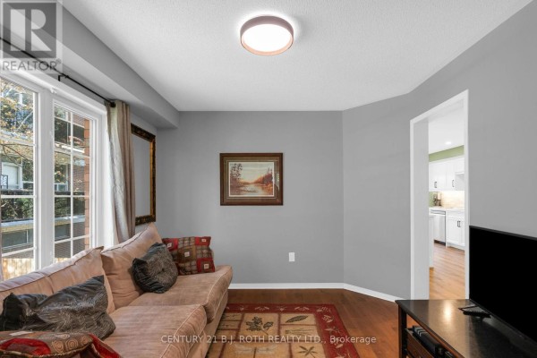 Living room with a sofa, patterned rug, artwork, and a large window with curtains. - 102 Holgate Street, Barrie
