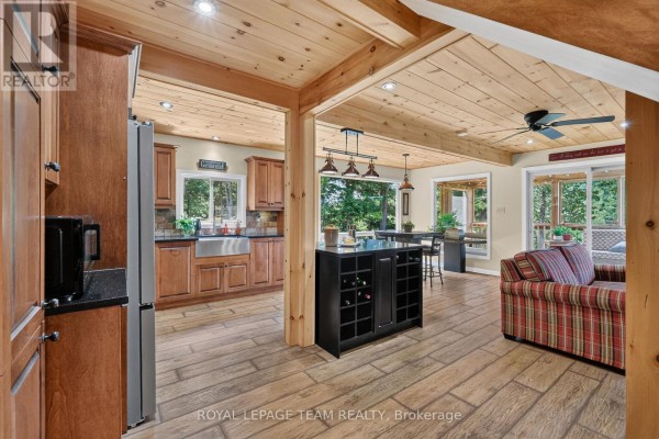 Open-concept living area with kitchen, island, dining area, and living room with plaid sofa. - 102 Mcvicar Lane, Mcnab/braeside
