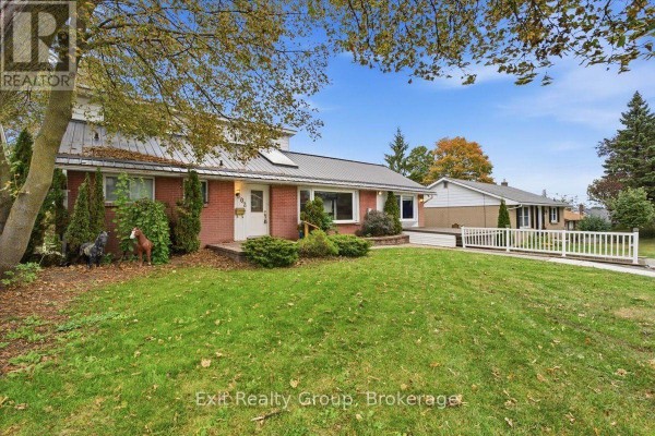 Side view of the brick house with a metal roof, green lawn, and trees. - 102 Orchard Drive, Belleville