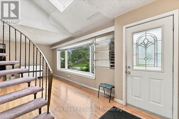 Interior view of the entrance hall with a curved carpeted staircase and a large bay window. - 102 Orchard Drive, Belleville