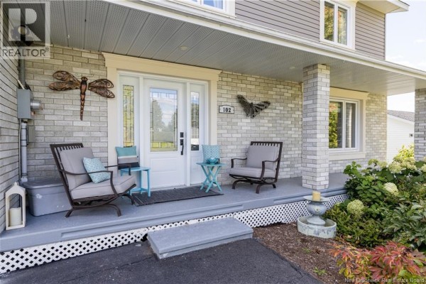 Covered front porch with two chairs, a small blue table, and dragonfly and butterfly wall decor. - 102 Plaisante Street, Drummond