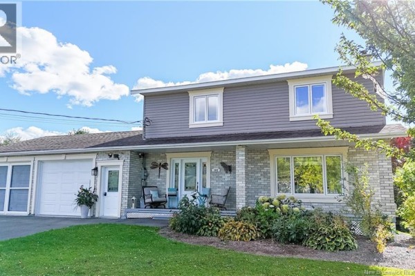 View of the house from the front yard showing the light gray siding, white-trimmed windows, and brick base. - 102 Plaisante Street, Drummond