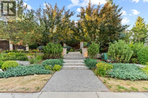 Stone steps leading to a house entrance with a paved walkway and mature landscaping in front. - 1020 Bel-aire Drive Sw, Calgary