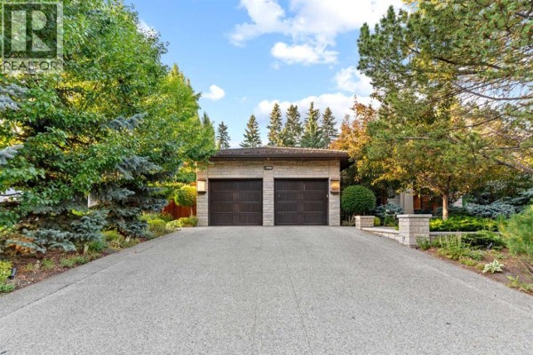 Double garage doors with stone accents on a detached garage, with trees and a paved driveway. - 1020 Bel-aire Drive Sw, Calgary