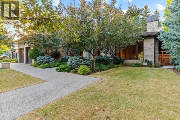 Side view of a house with stone exterior and large windows, surrounded by grass and trees. - 1020 Bel-aire Drive Sw, Calgary