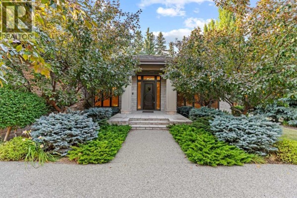 Paved walkway leading to a house entrance with double doors and a stone facade, framed by lush greenery. - 1020 Bel-aire Drive Sw, Calgary