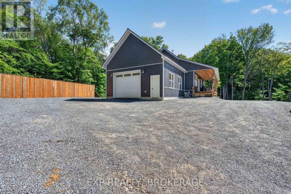 View of the attached garage with a white overhead door, dark siding, and a covered porch area. - 1020 Hill Road, Frontenac