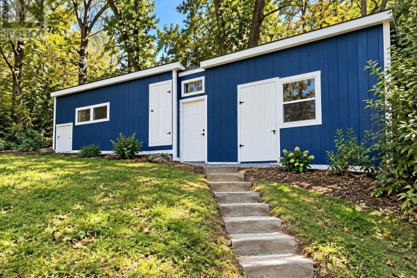A long, blue structure with white doors and windows, accessed by concrete steps on a grassy slope. - 1020 Kellar Road, Frontenac